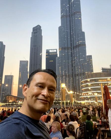 Gustavo en camiseta frente al Burj Khalifa, al atardecer
