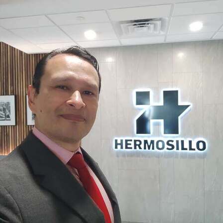 Gustavo en las oficinas de Grupo Hermosillo, junto al logotipo de la empresa